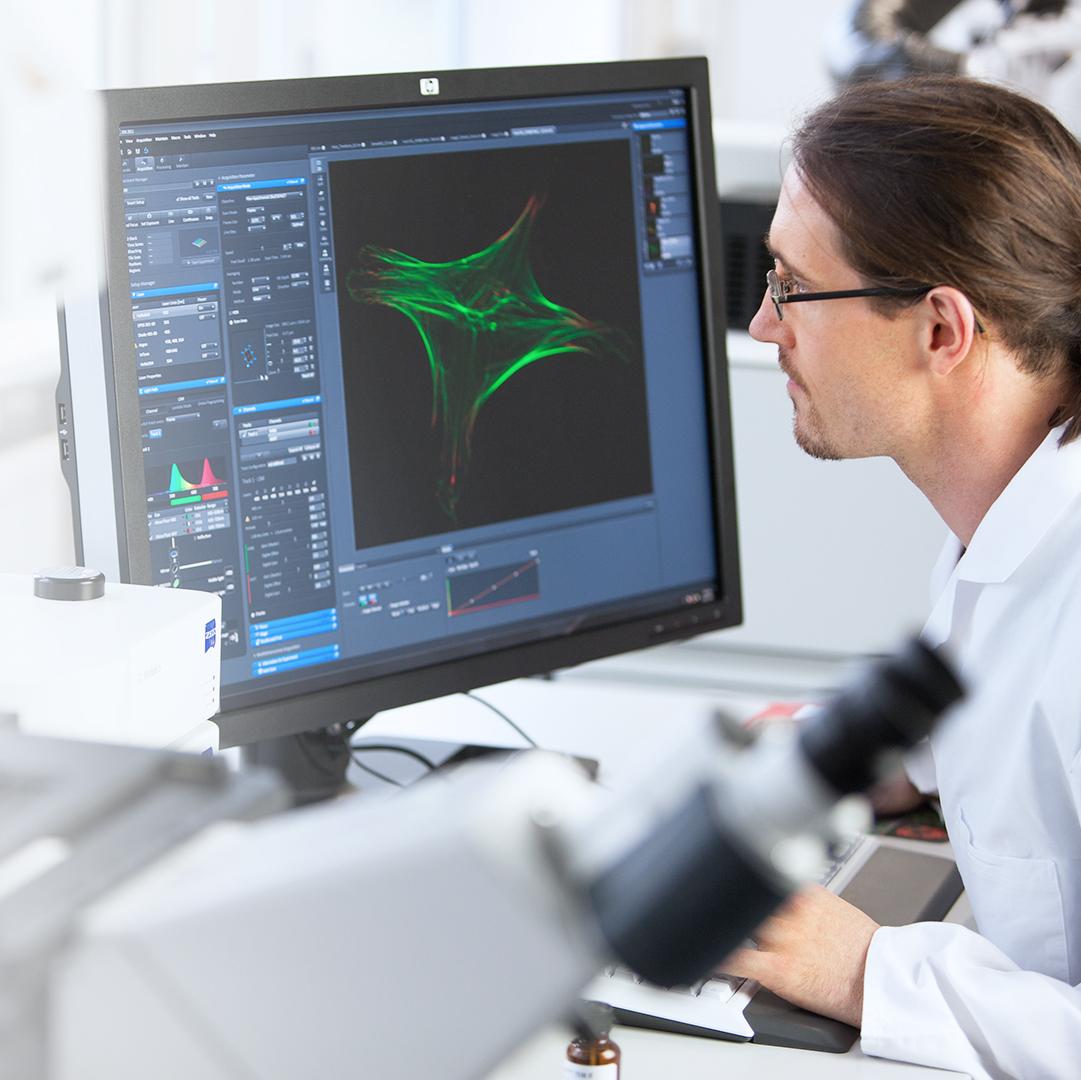 Scientist analyzing microscopic data on a computer screen in a laboratory setting, with a microscope in the foreground